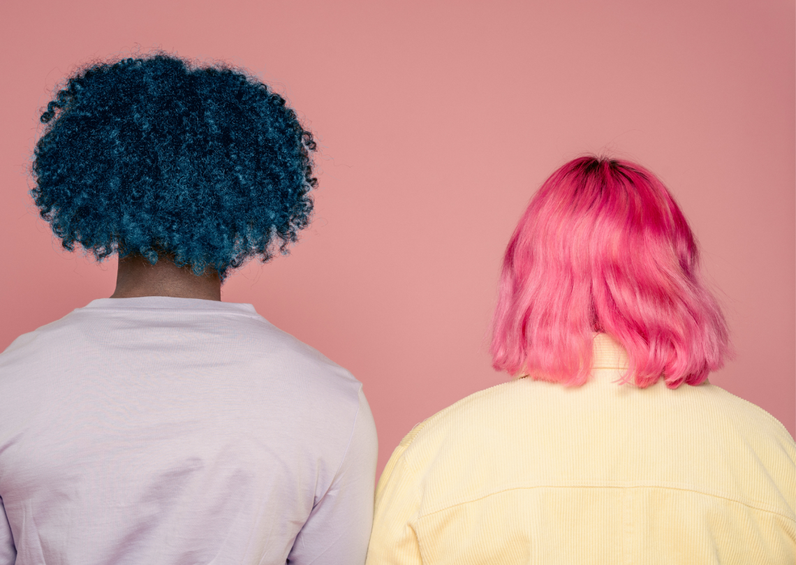 duas pessoas de costas com cabelos coloridos, a da esquerda é azul e a da direita é rosa